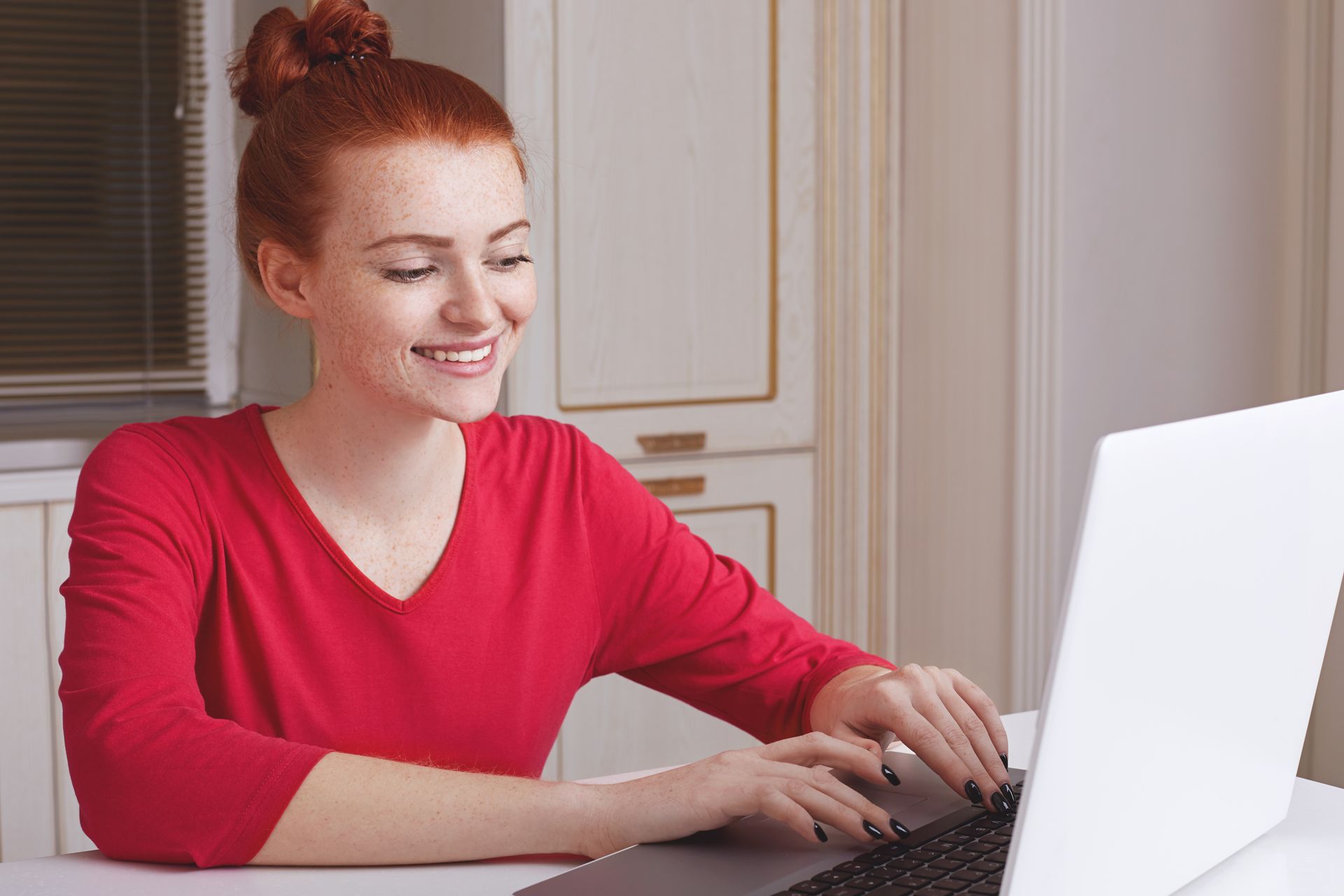 A woman is sitting at a table typing on a laptop computer.