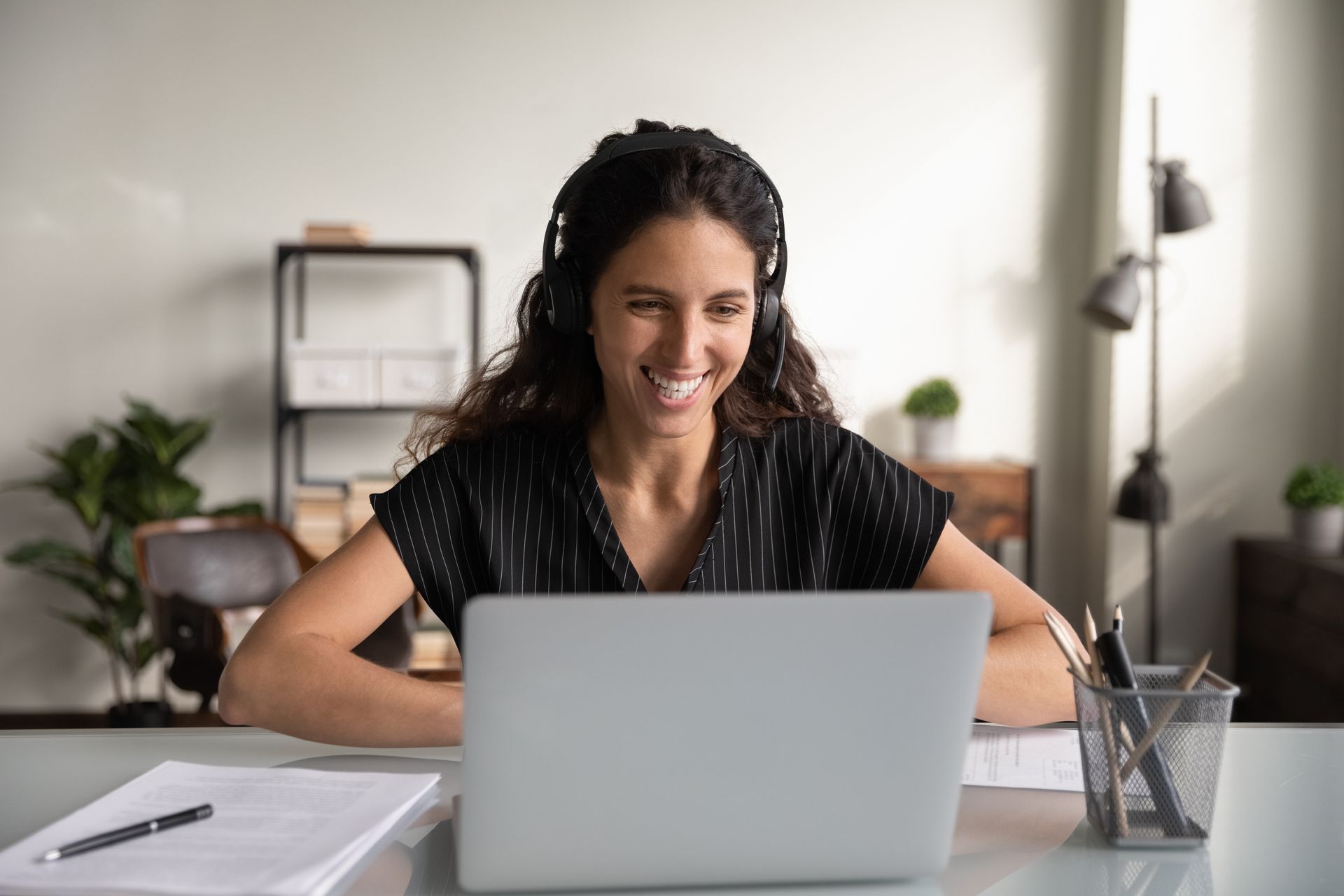 A woman wearing headphones is sitting at a desk using a laptop computer.