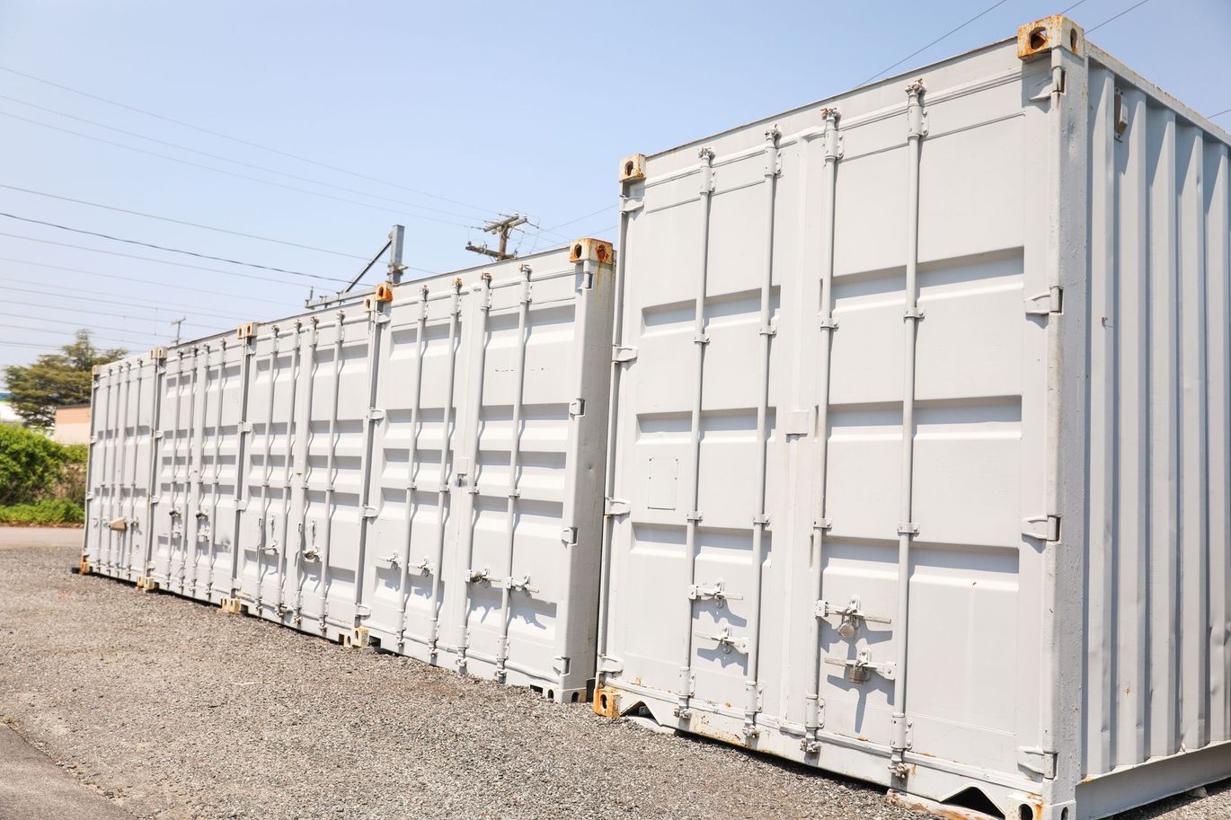 A row of shipping containers are lined up in a gravel lot.