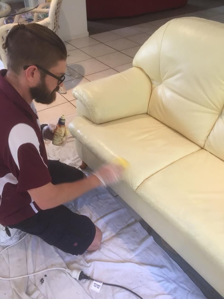 A Man is Sitting on the Floor Painting a White Leather Couch — Abbsolve Services in Peregian Beach, QLD