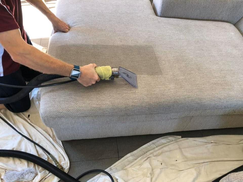 A Man is Cleaning a Couch With a Vacuum Cleaner — Abbsolve Services in Nambour, QLD