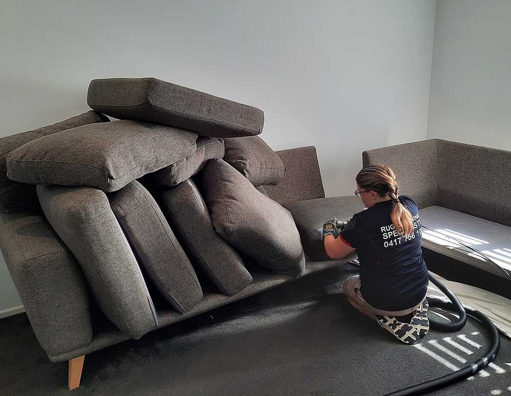 A Woman is Cleaning a Couch With a Vacuum Cleaner in a Living Room — Abbsolve Services in Cooroy, QLD
