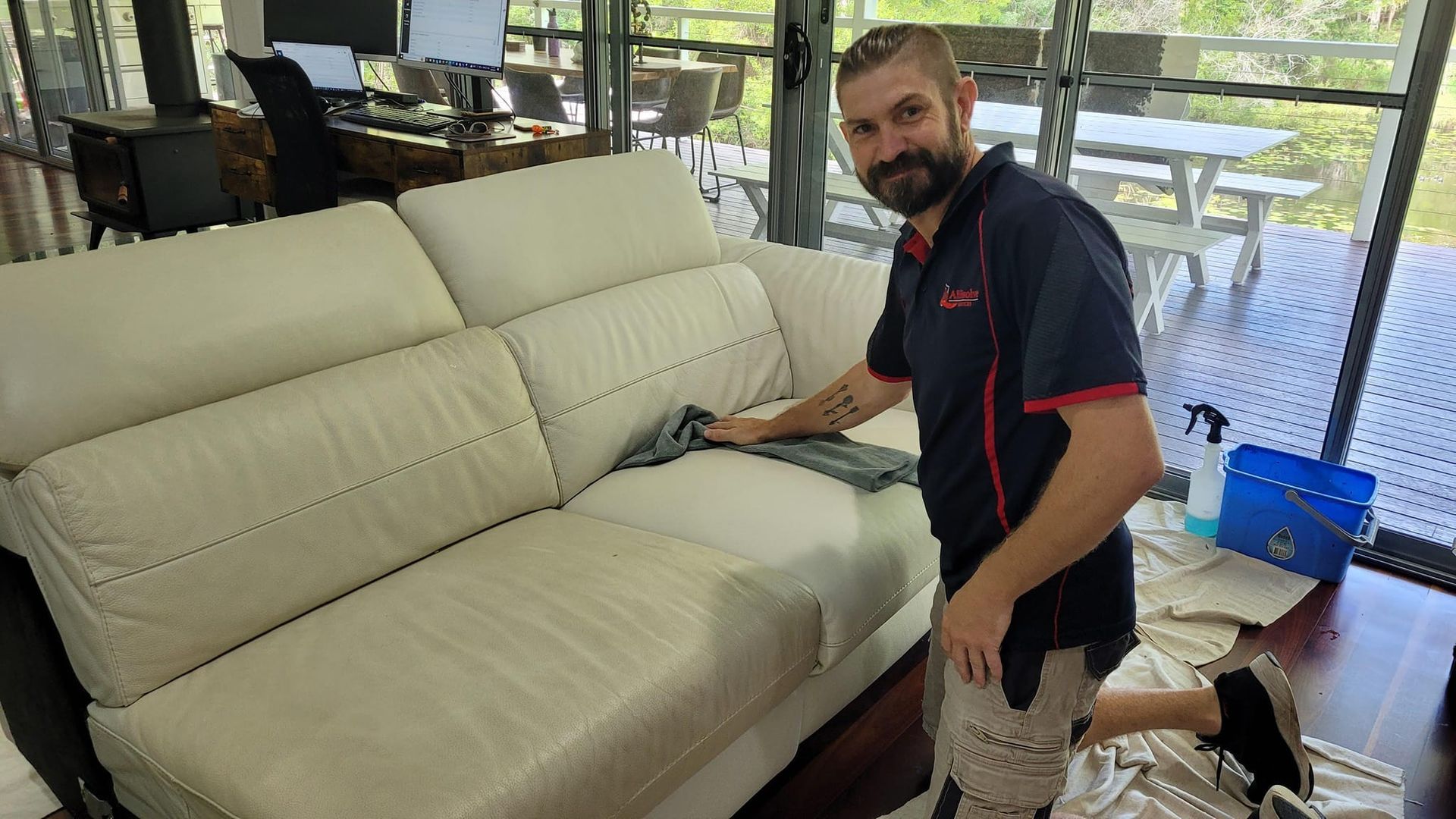 Man Cleaning A Beige Leather Sofa On A Wooden Deck, Smiling, In A Home Setting