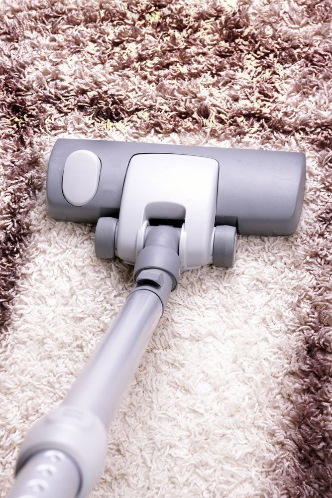 A vacuum cleaner head moving over a shaggy rug, showing a clear contrast between clean and dirty.