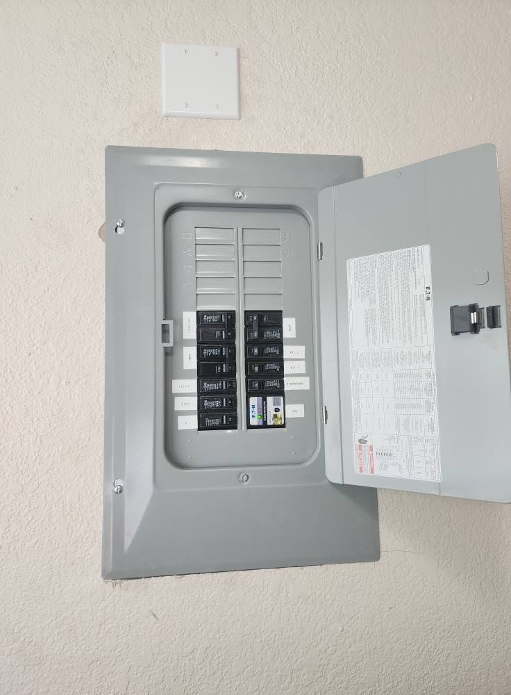 Electrical circuit breaker panel with the door open, mounted on a beige wall.