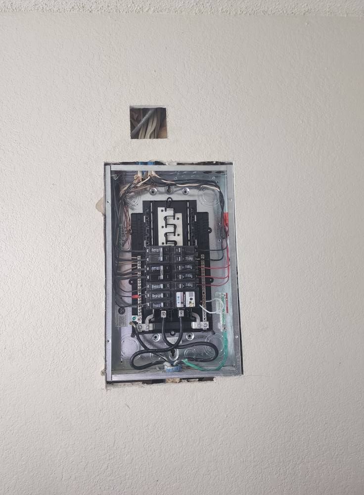 Electrical breaker box on a beige wall, partially uncovered with wires visible.