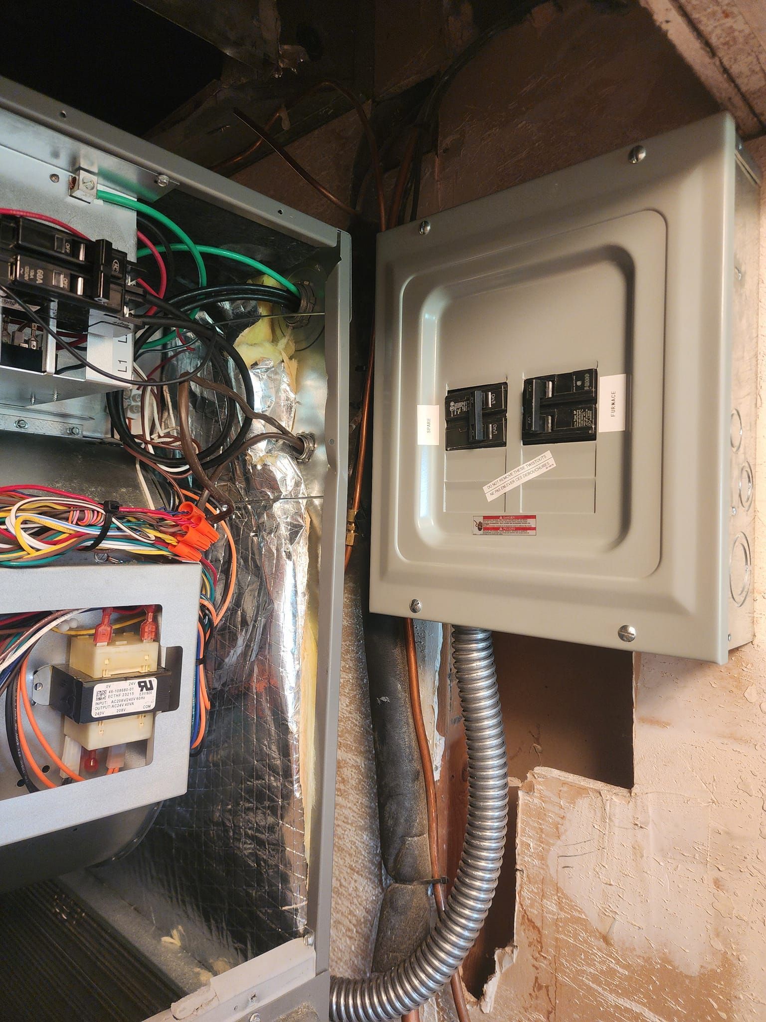 Electrical panel and wiring in a wall. Gray metal box, silver foil insulation, conduit, exposed wires.