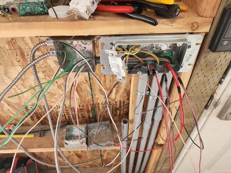 Electrical wiring in open boxes on wood, with exposed wires of various colors.