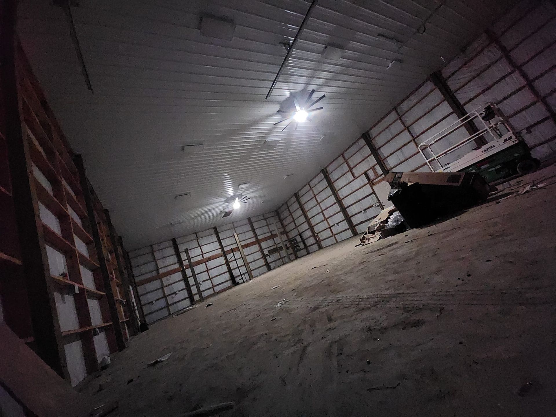 Interior of a large, empty warehouse with metal walls and ceiling; dirt floor.
