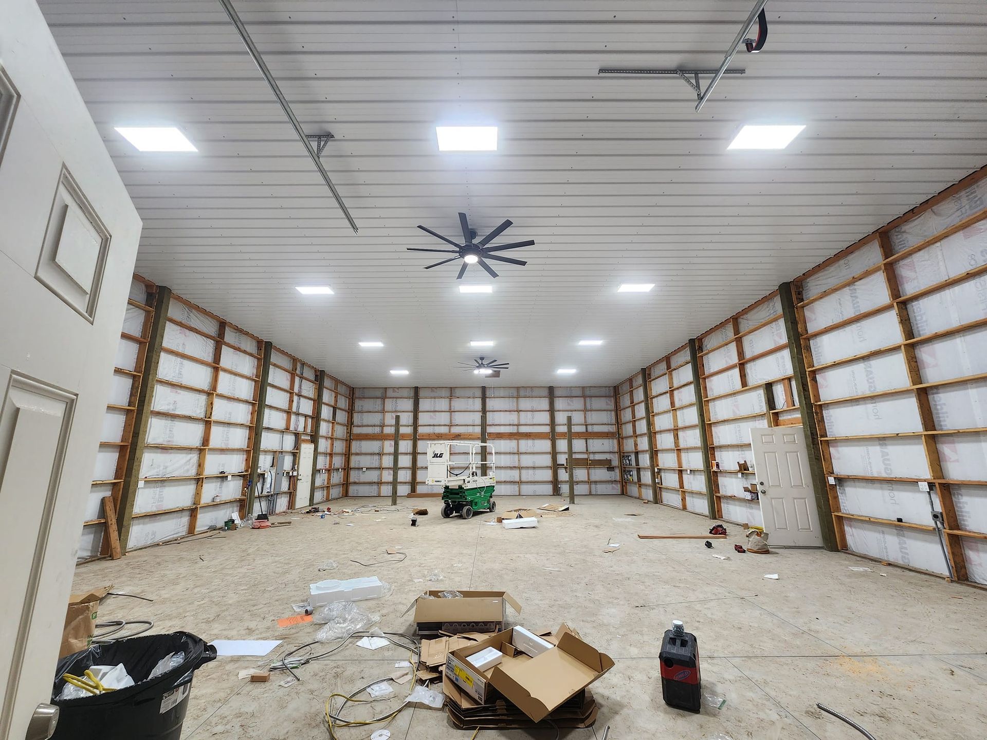 Inside of a large, unfinished warehouse with exposed wood framing, concrete floor, and overhead lighting.