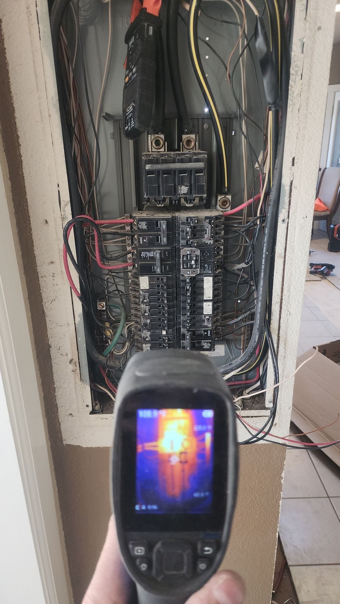 Infrared camera showing heat in an electrical panel, held by a hand. High heat indicated on a circuit breaker.