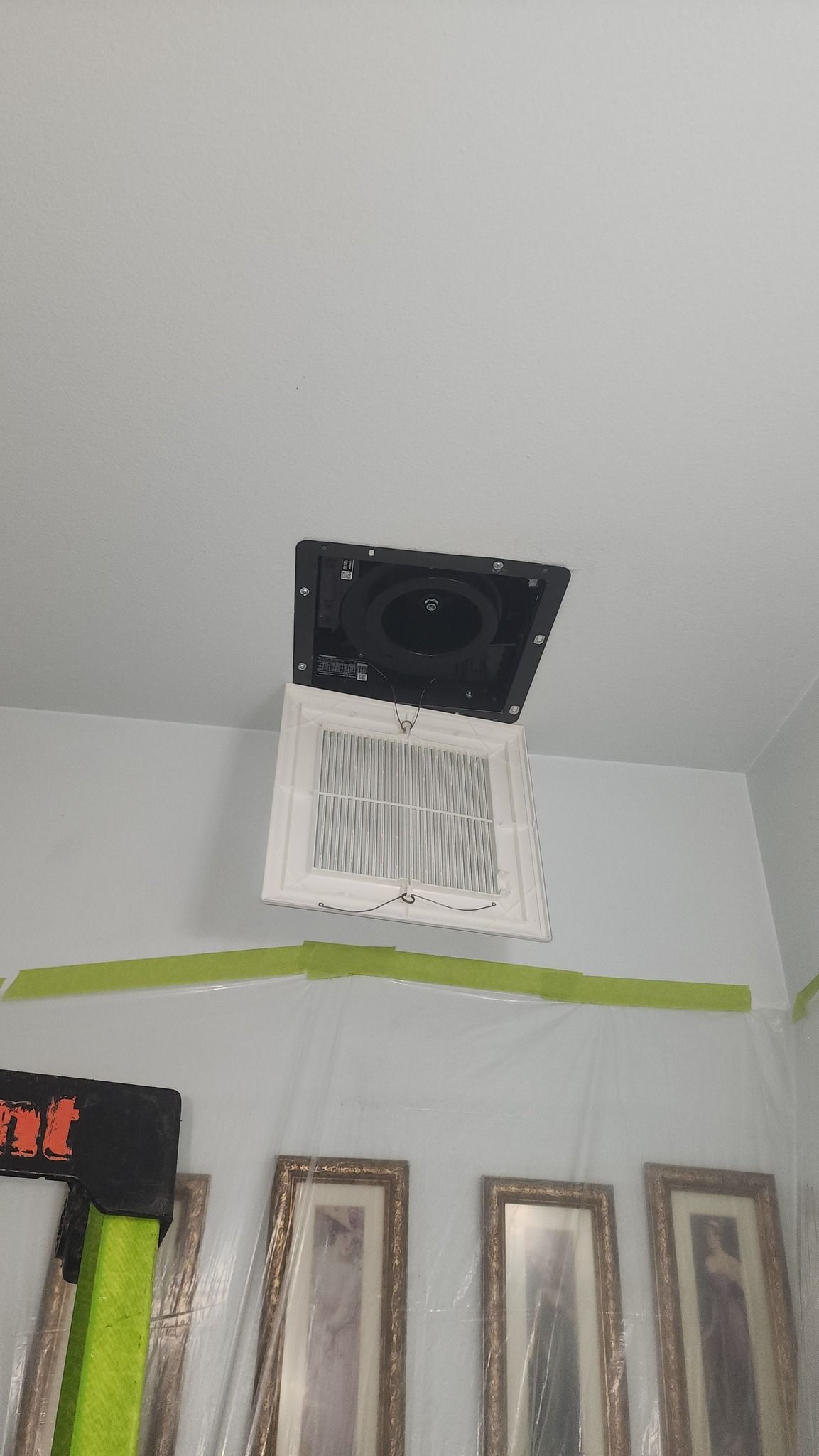 Ceiling vent with air conditioning unit. White wall with green tape.  Artwork on wall below.