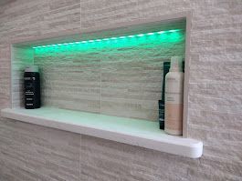 Recessed shower shelf with green LED lighting, containing toiletries against a tiled wall.