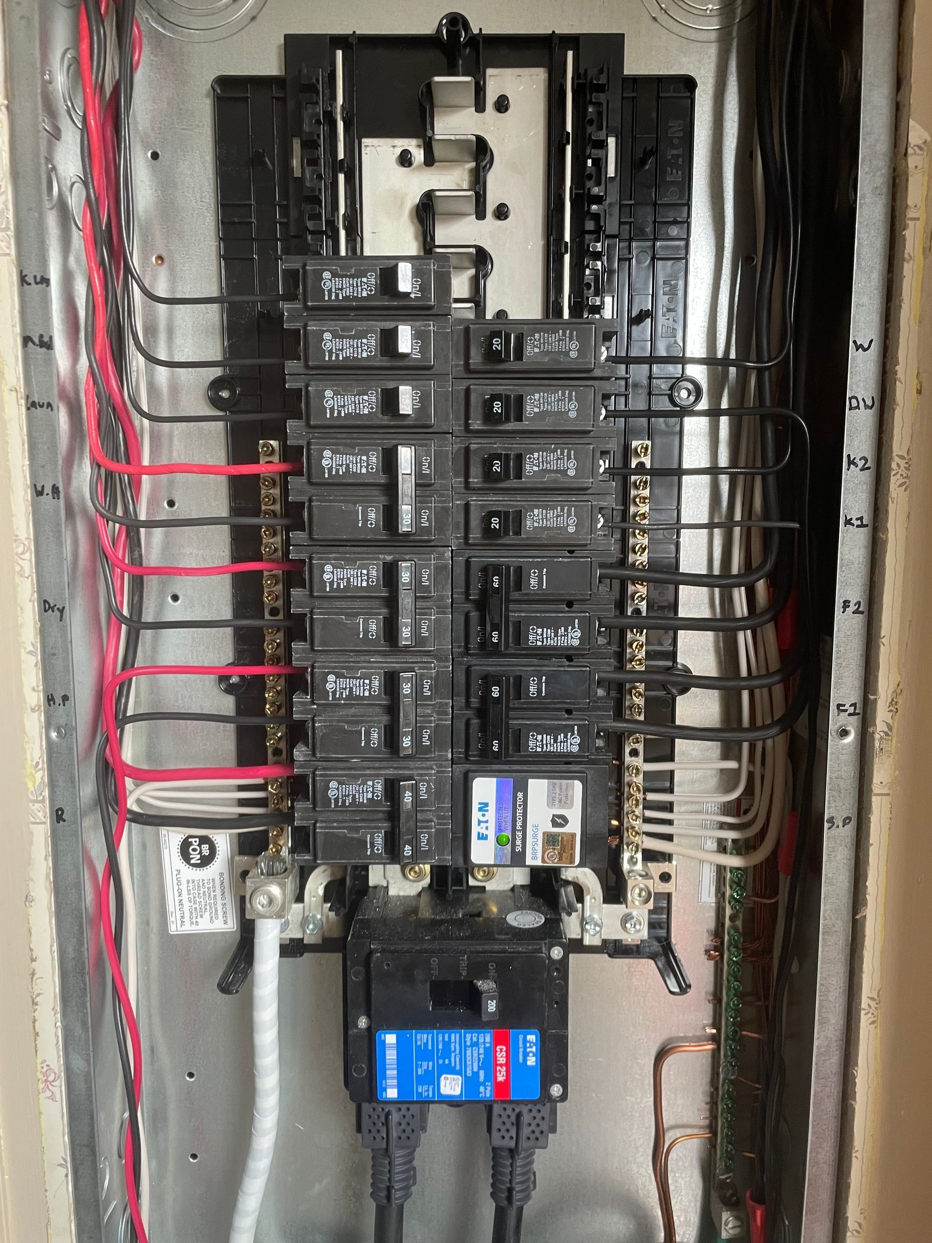 Electrical panel with multiple circuit breakers and wires. Black and gray breakers, red and white wires, metal panel.
