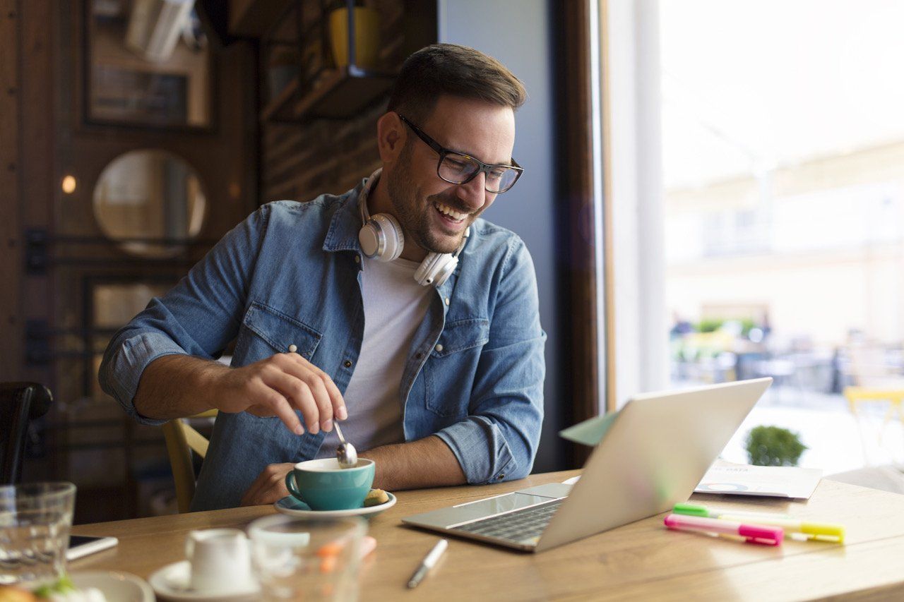A man is sitting at a table with a laptop and a cup of coffee.