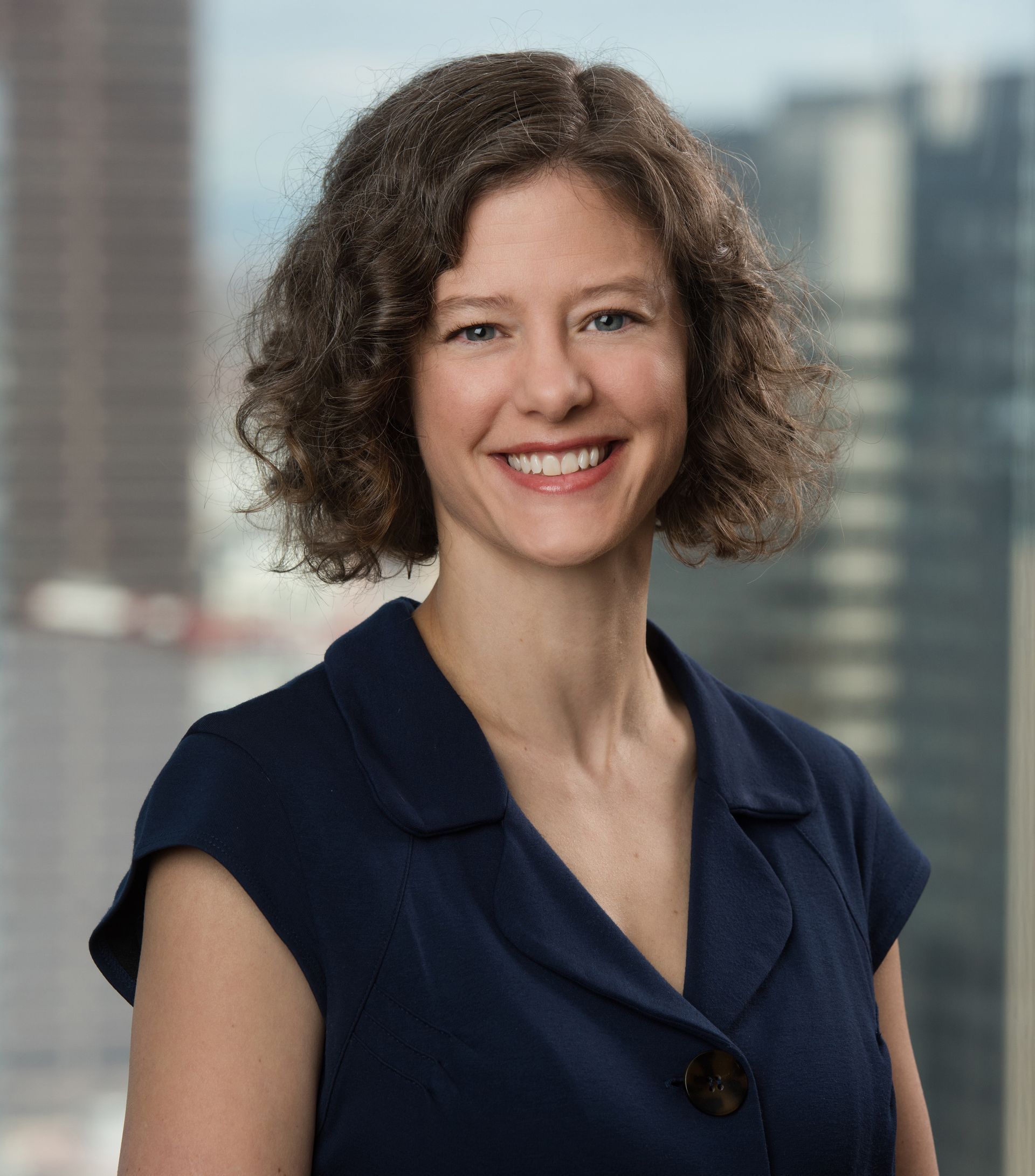 A woman with curly hair is smiling in front of a city skyline.