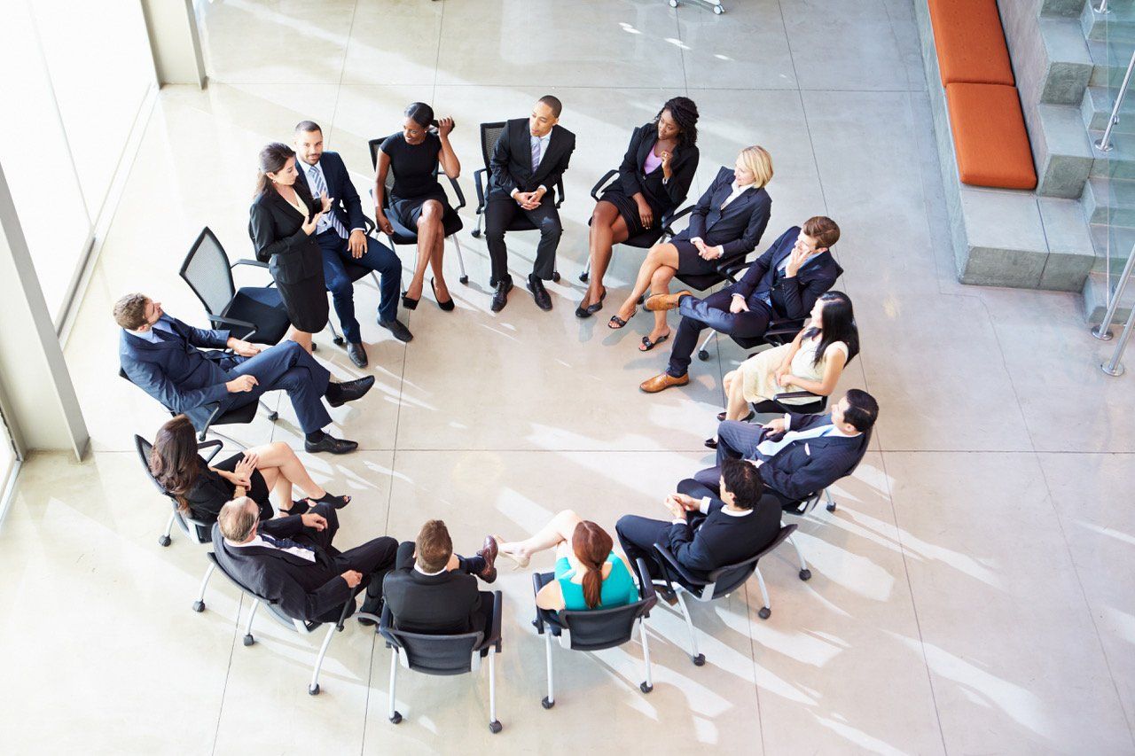 A group of business people are sitting in a circle in an office.