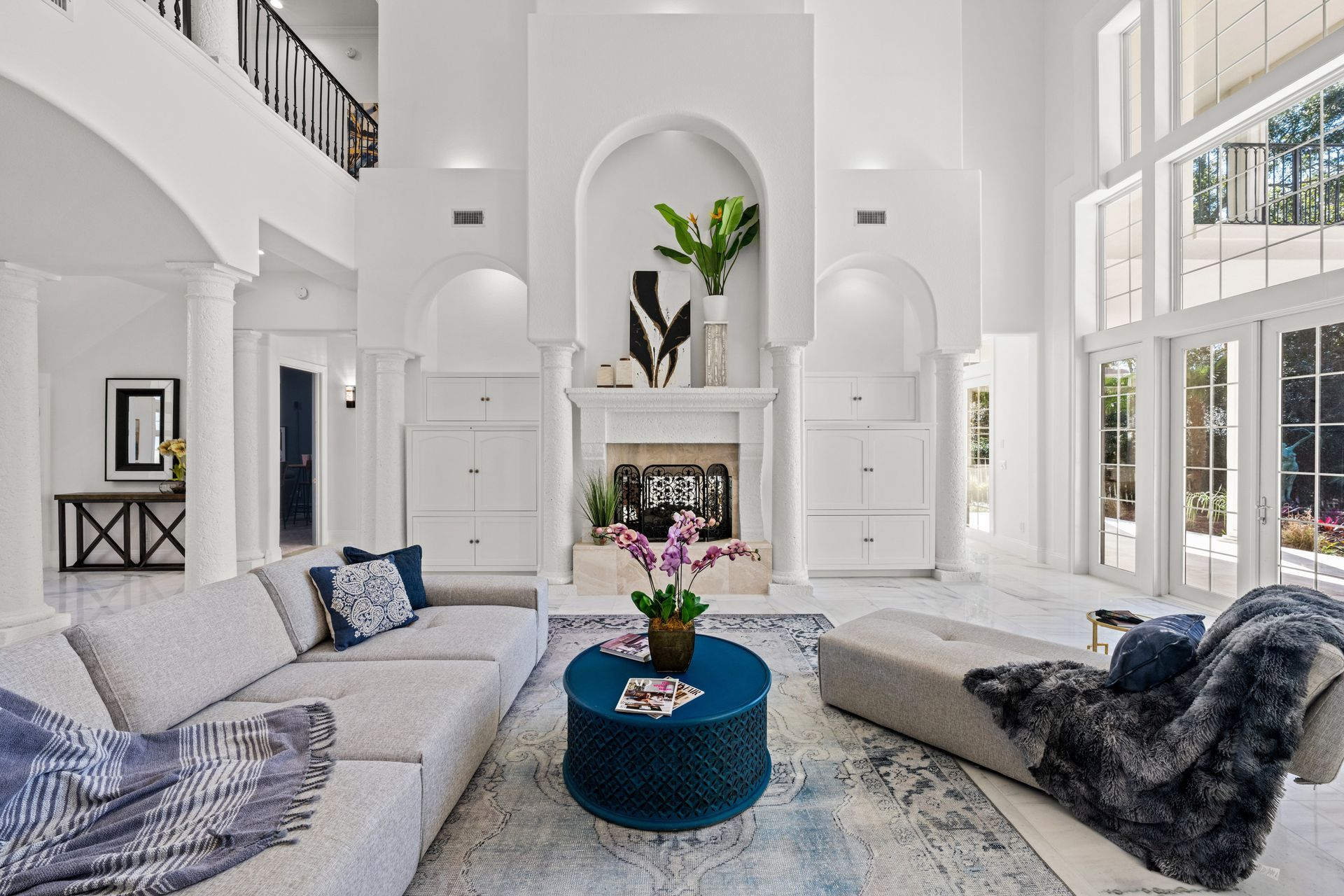 Spacious white living room with high ceilings, arched details, fireplace, and large windows.