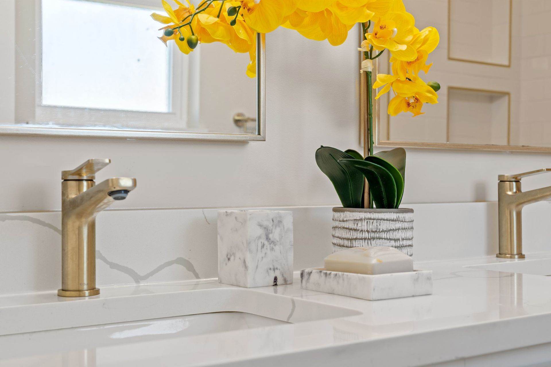 Gold faucets, white countertop, and decorative flowers in a bright bathroom.
