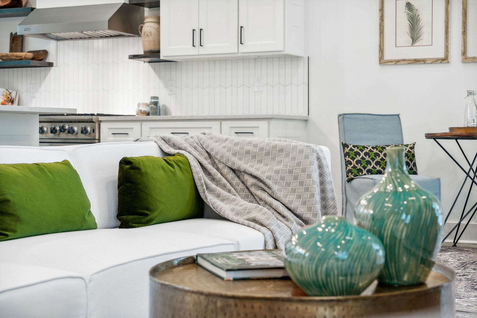 White couch with green pillows, teal vases on a round coffee table in a modern kitchen.