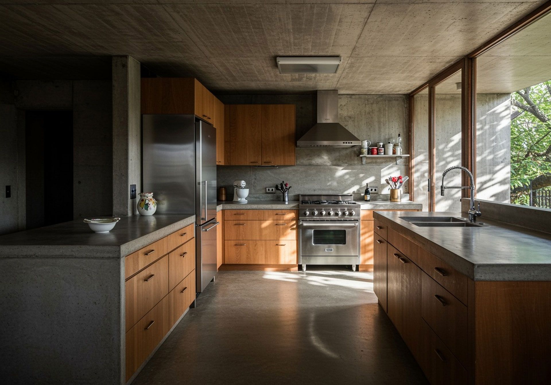 Modern kitchen with concrete countertops, wood cabinets, stainless steel appliances, and large windows.
