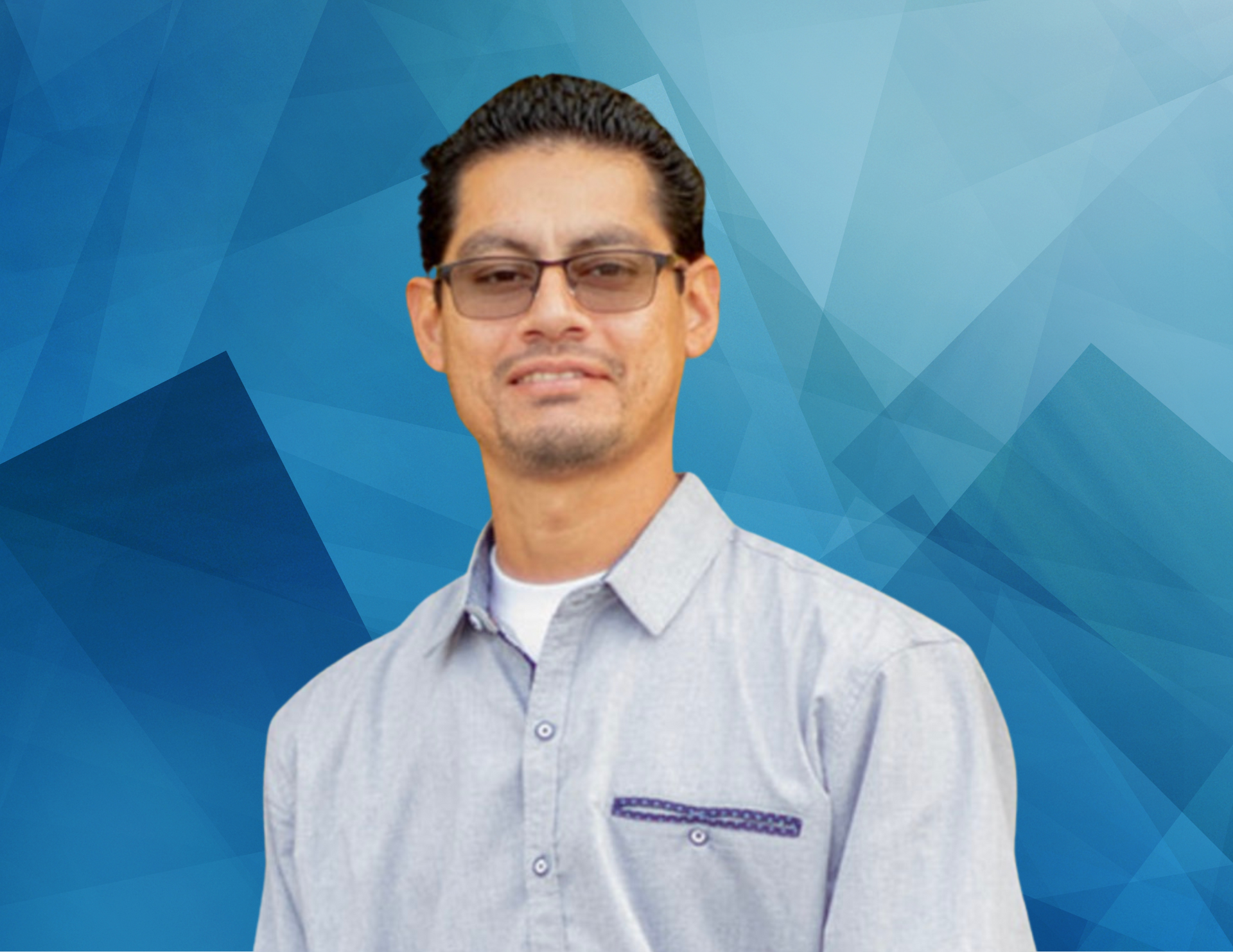 A man wearing glasses and a grey shirt is standing in front of a blue background.