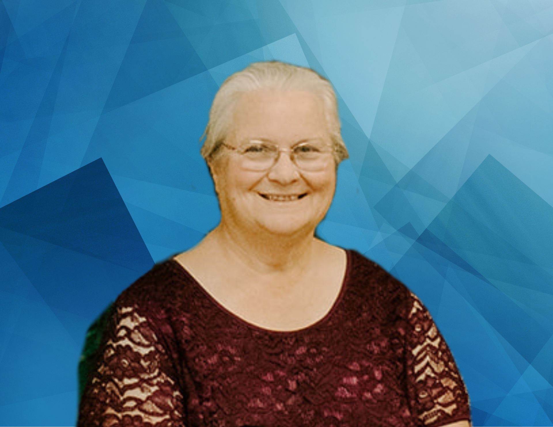An elderly woman wearing glasses and a red top is smiling in front of a blue background.