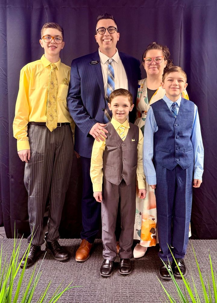 A family of five posing for a formal portrait against a dark backdrop. They are dressed in business attire.