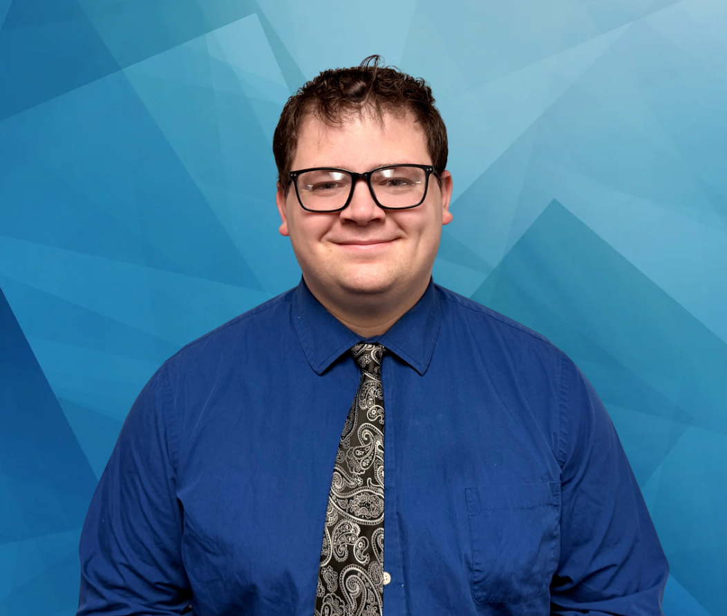 A young man wearing glasses and a red jacket and tie is smiling.