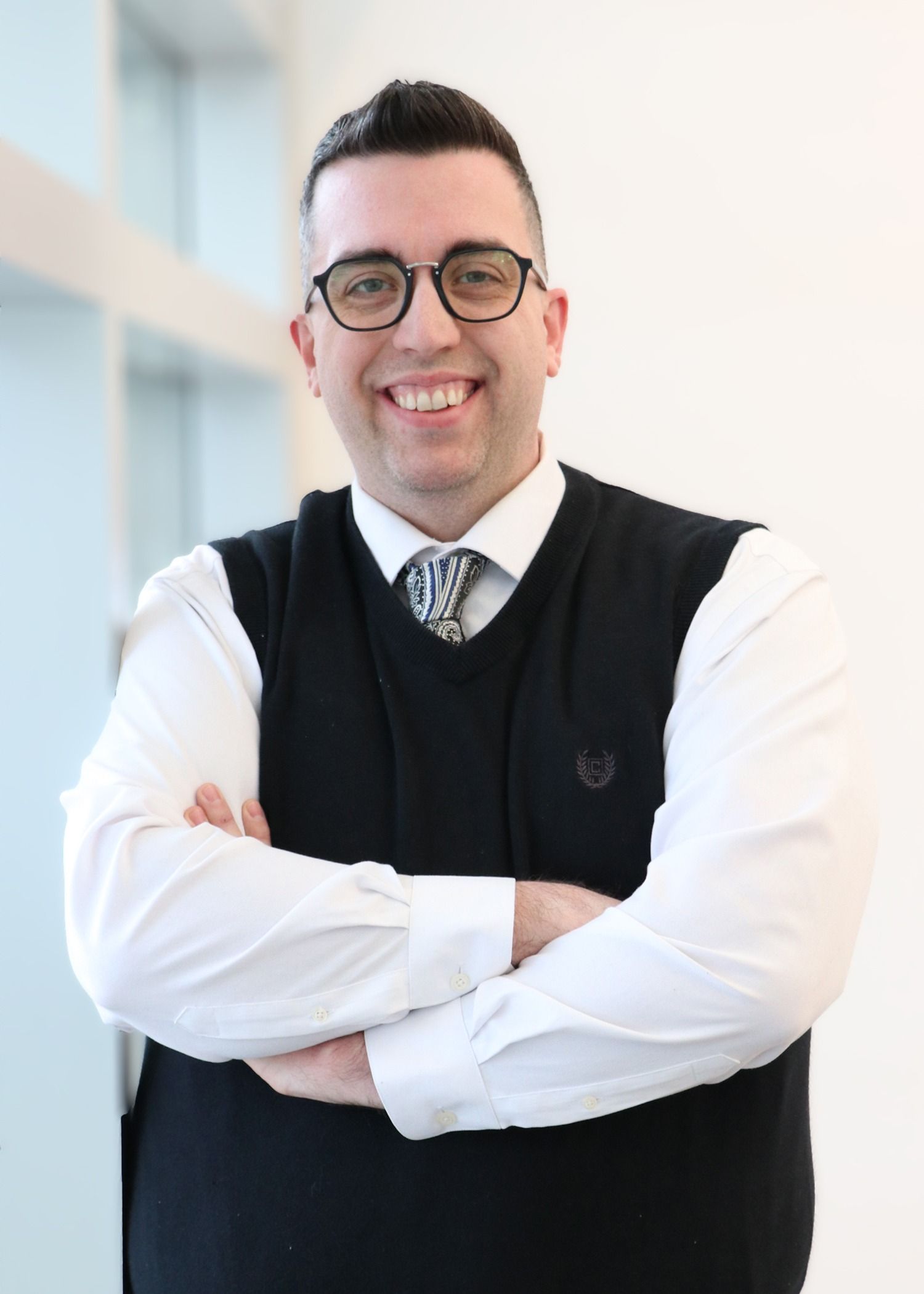 A man in a suit and glasses is smiling with his arms crossed.