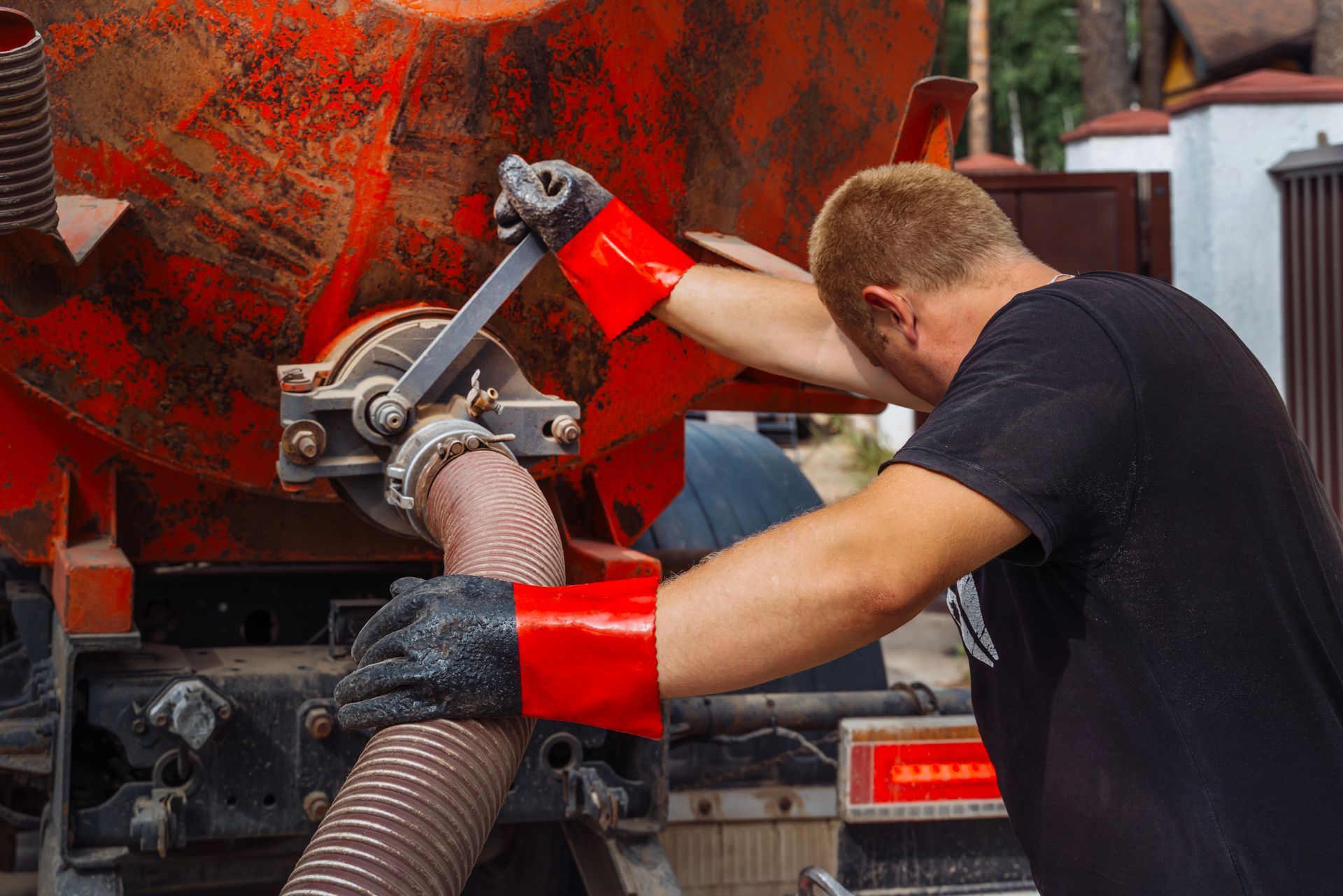 Worker connecting hose to commercial waste truck during industrial cleanup.