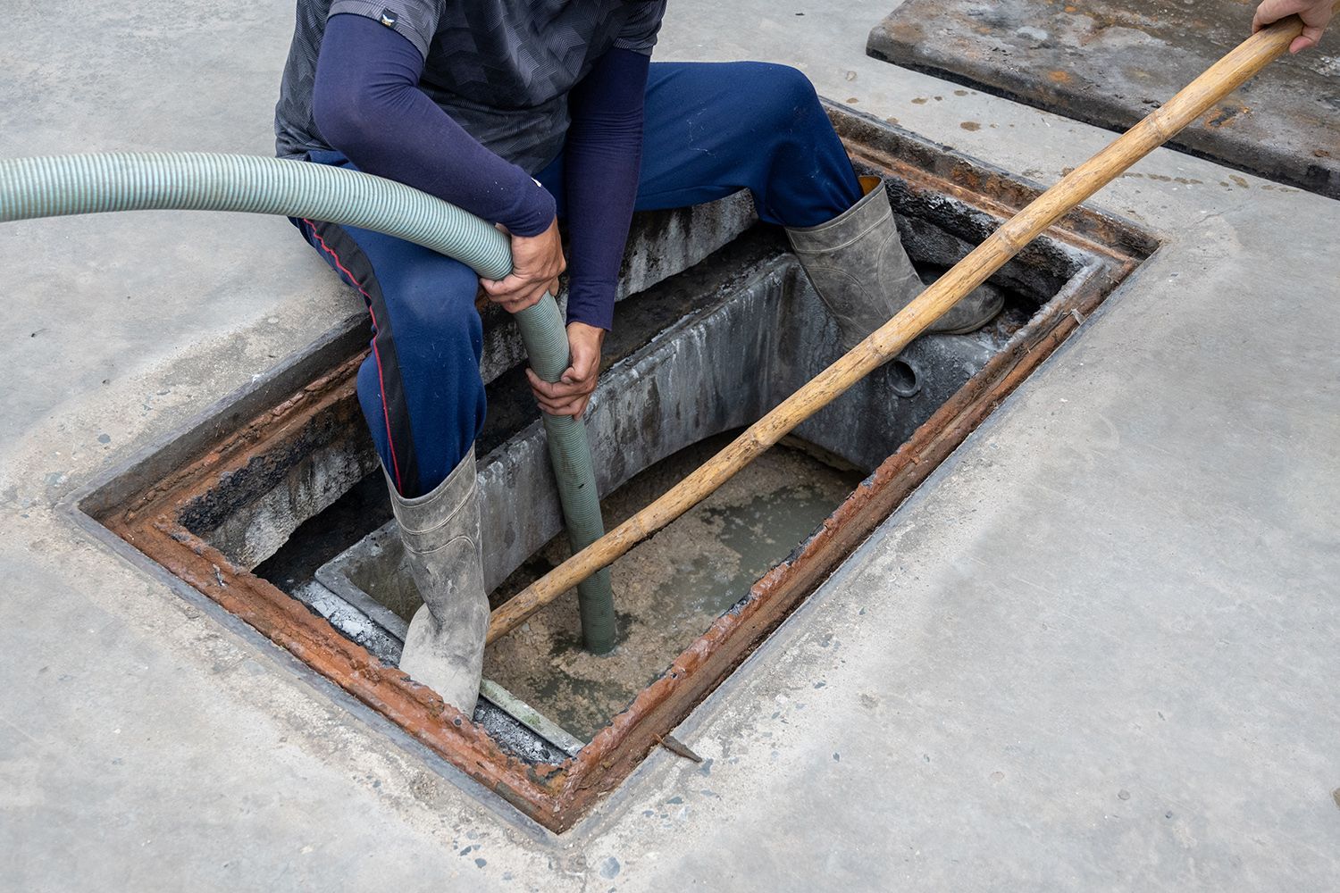 A man cleaning a septic system with hoses and tools on a concrete floor area outside