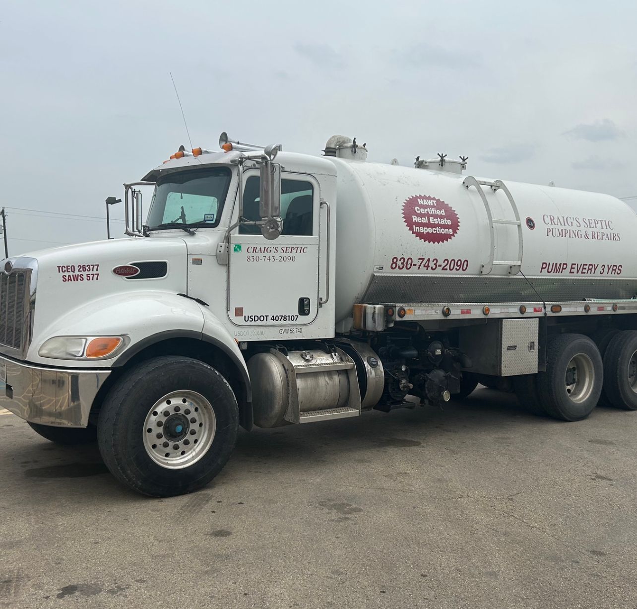 A blue septic truck parked on a residential street with hose extended, sunny day.