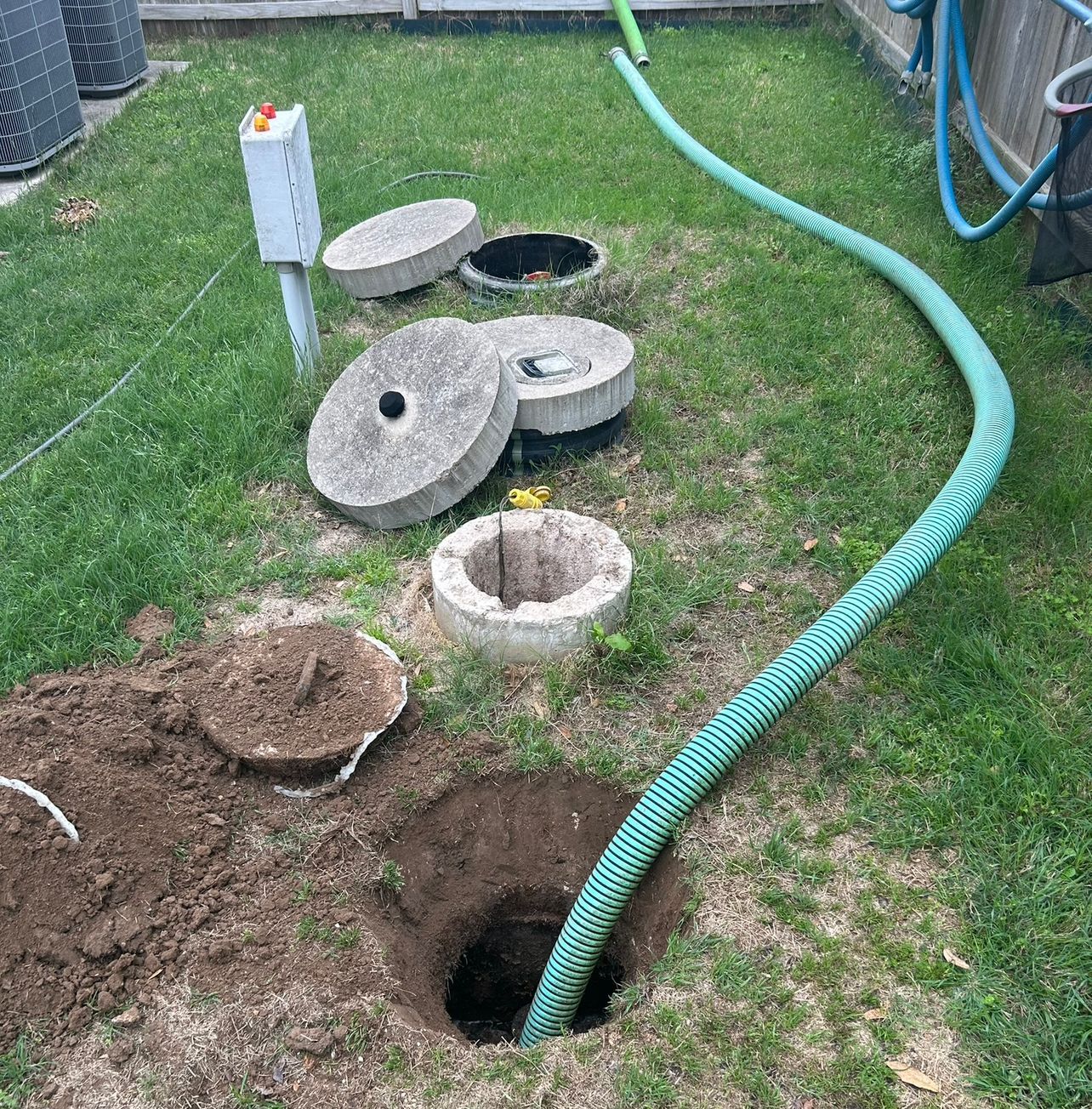 View into a dark manhole with a hose and metal ladder visible.
