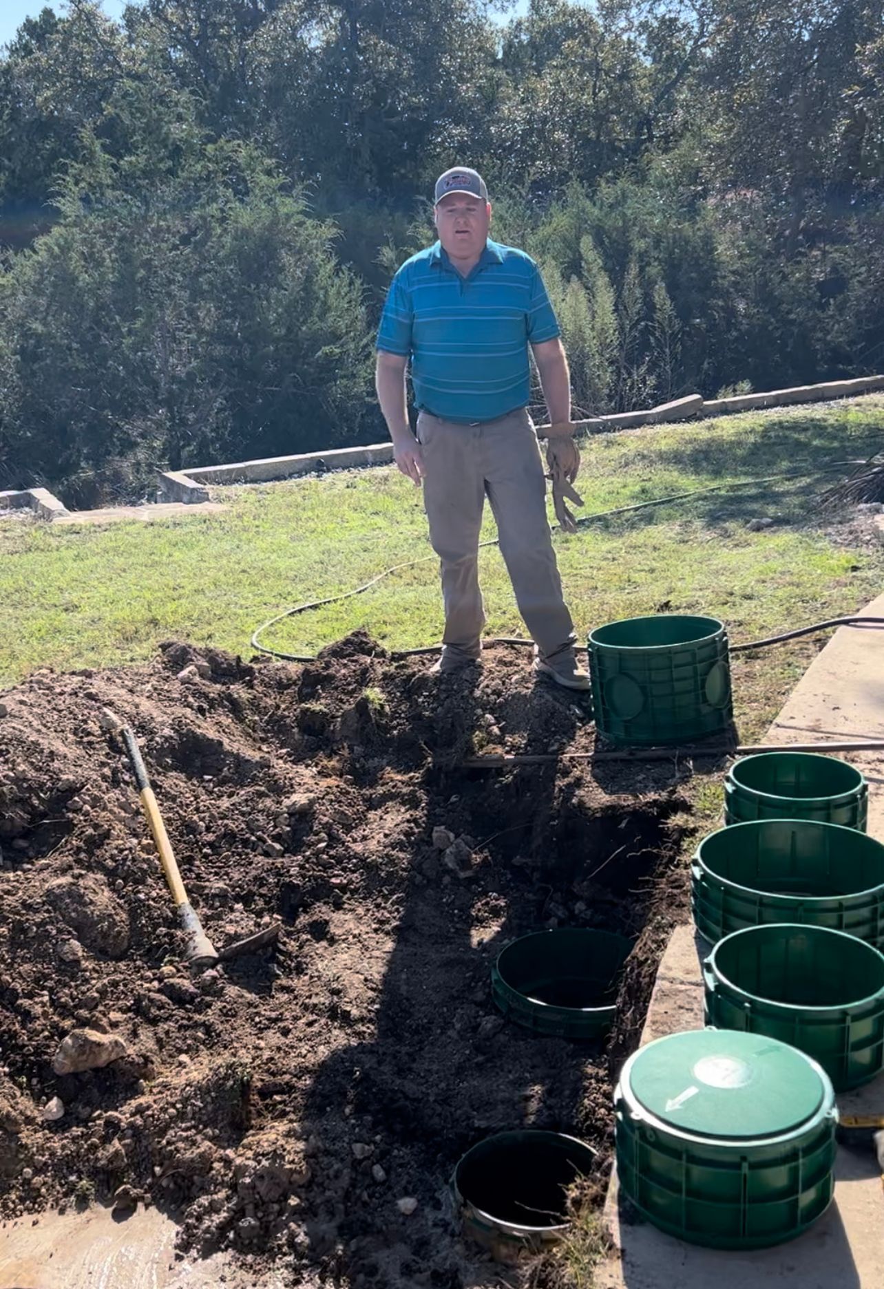 Hose inserted into an open septic tank, removing waste. Green concrete, brown hose, and debris in a yard.