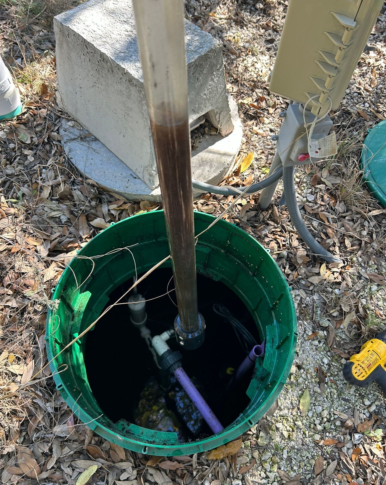 Person lowering a submersible pump into an open septic tank in a yard.