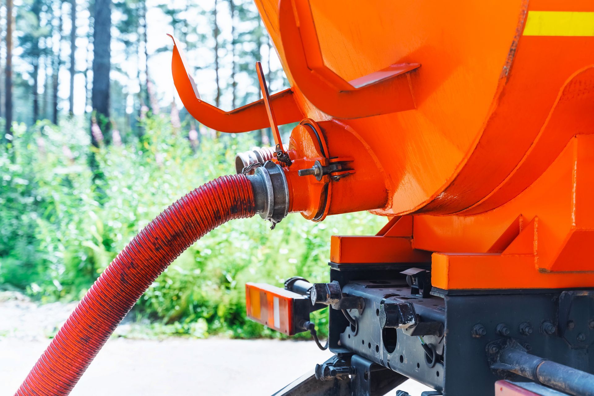 Orange tank truck detail with a red hose connected, set in a forest.