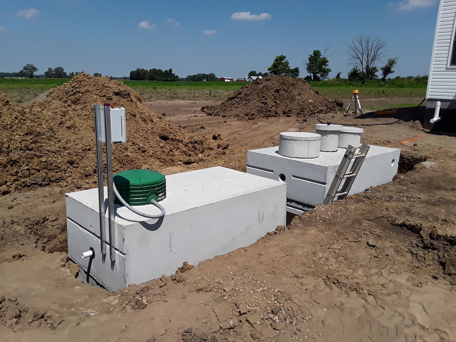 Concrete septic tanks being installed in a dirt field under a bright blue sky.