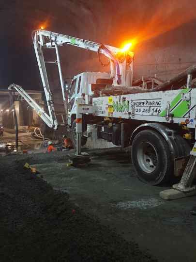 White concrete pump truck at a construction site near buildings.