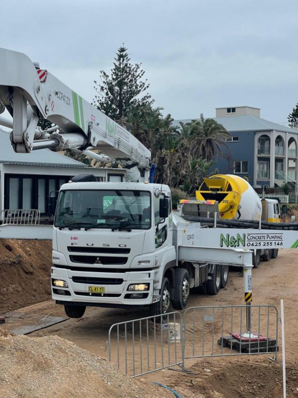 White concrete pump truck at a construction site near buildings.