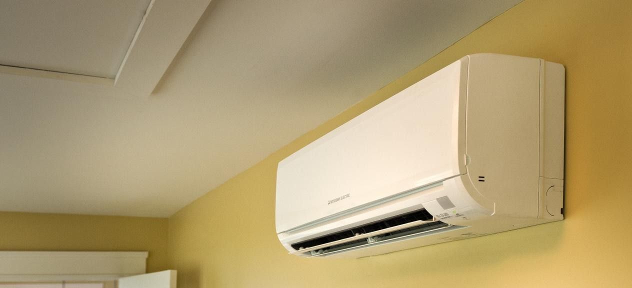 A white air conditioner is hanging on a yellow wall in a room.
