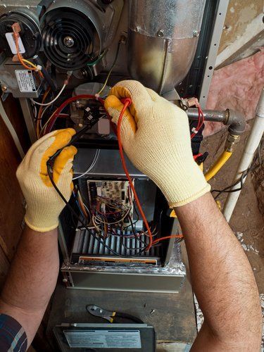 A man wearing yellow gloves is working on a heating system.