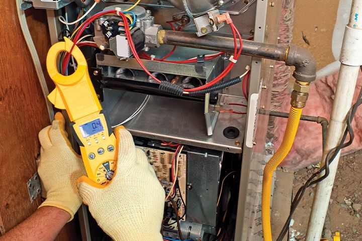 A person is working on a heating system with a clamp meter.