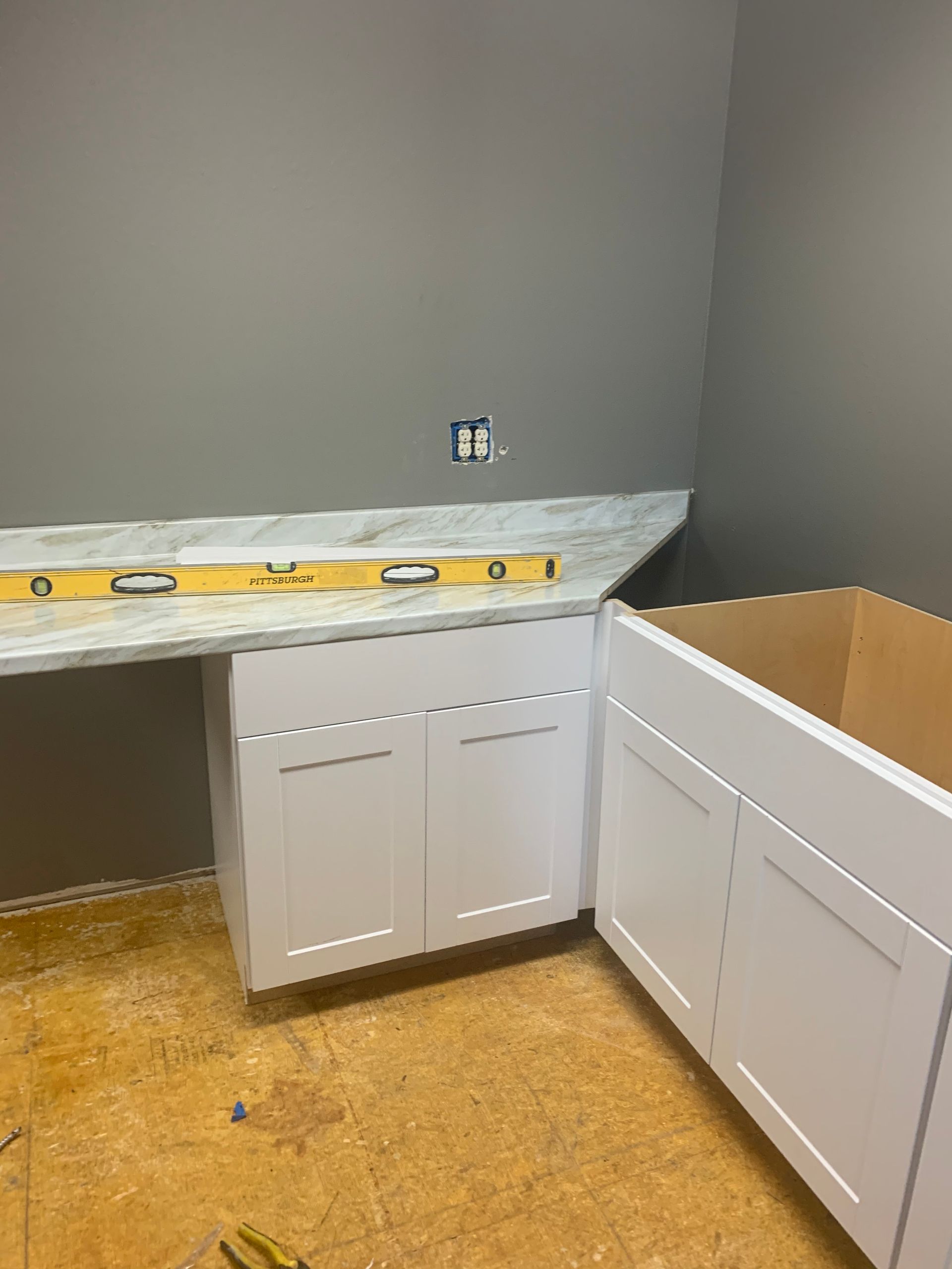 A kitchen is being remodeled with white cabinets and a marble counter top.