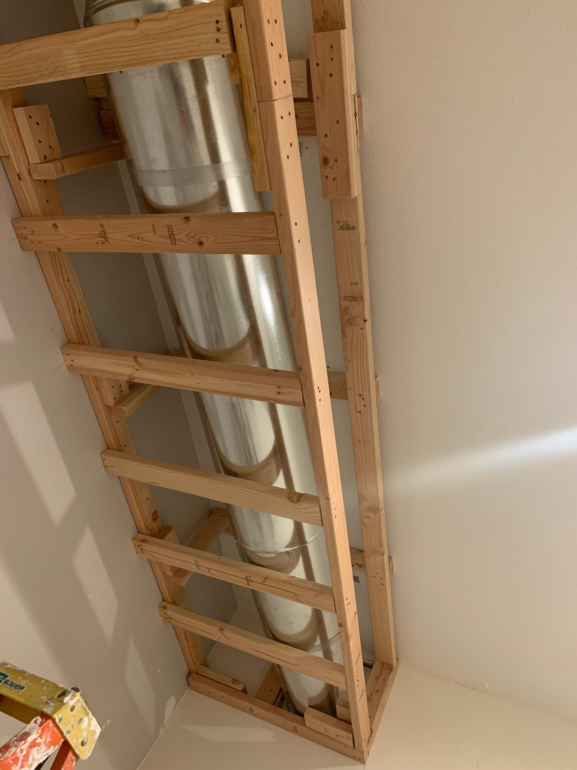A wooden ladder is sitting next to a metal pipe in a room.