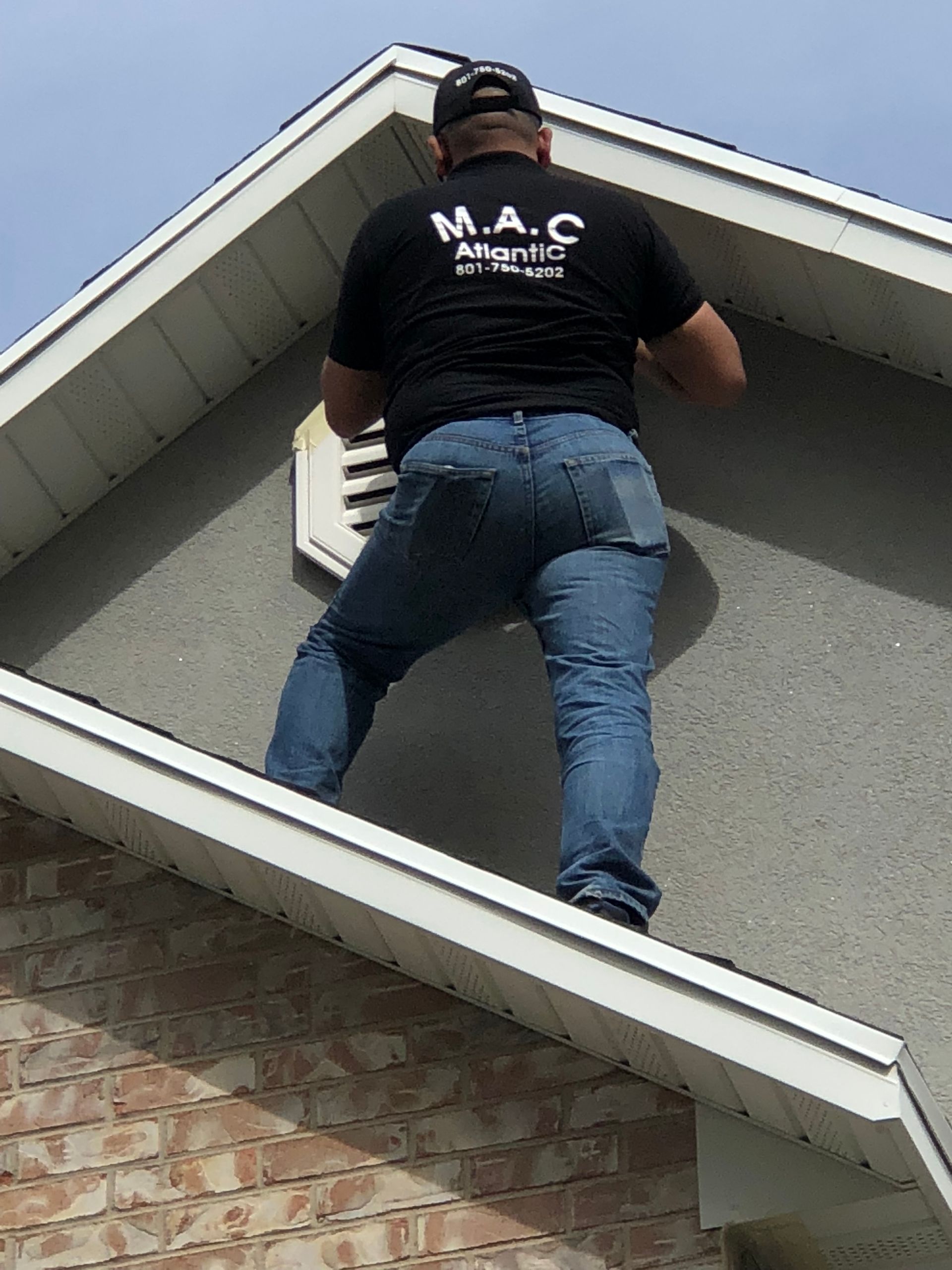A man wearing a mac shirt is standing on the roof of a house