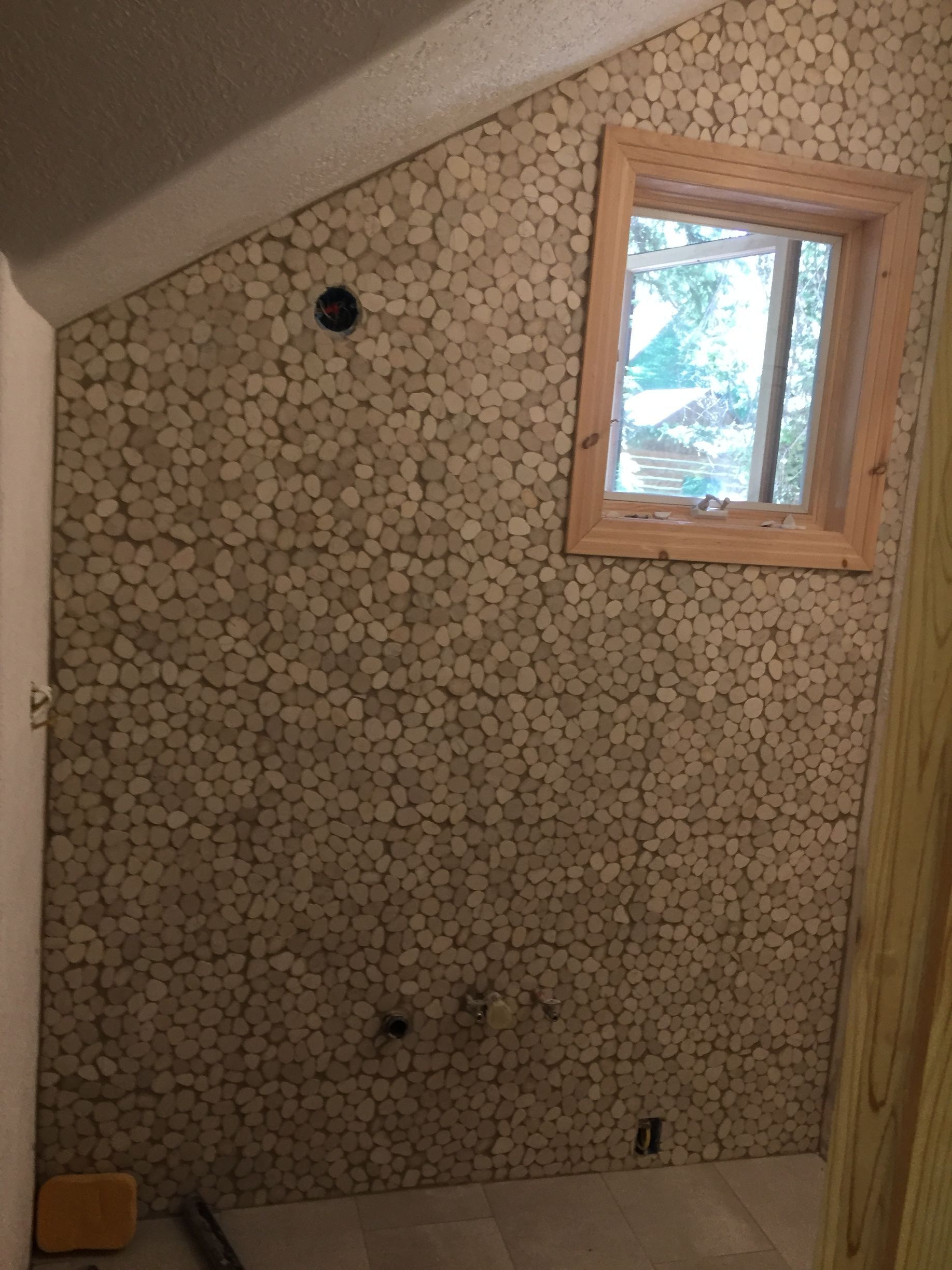 A bathroom with a tiled wall and a window.