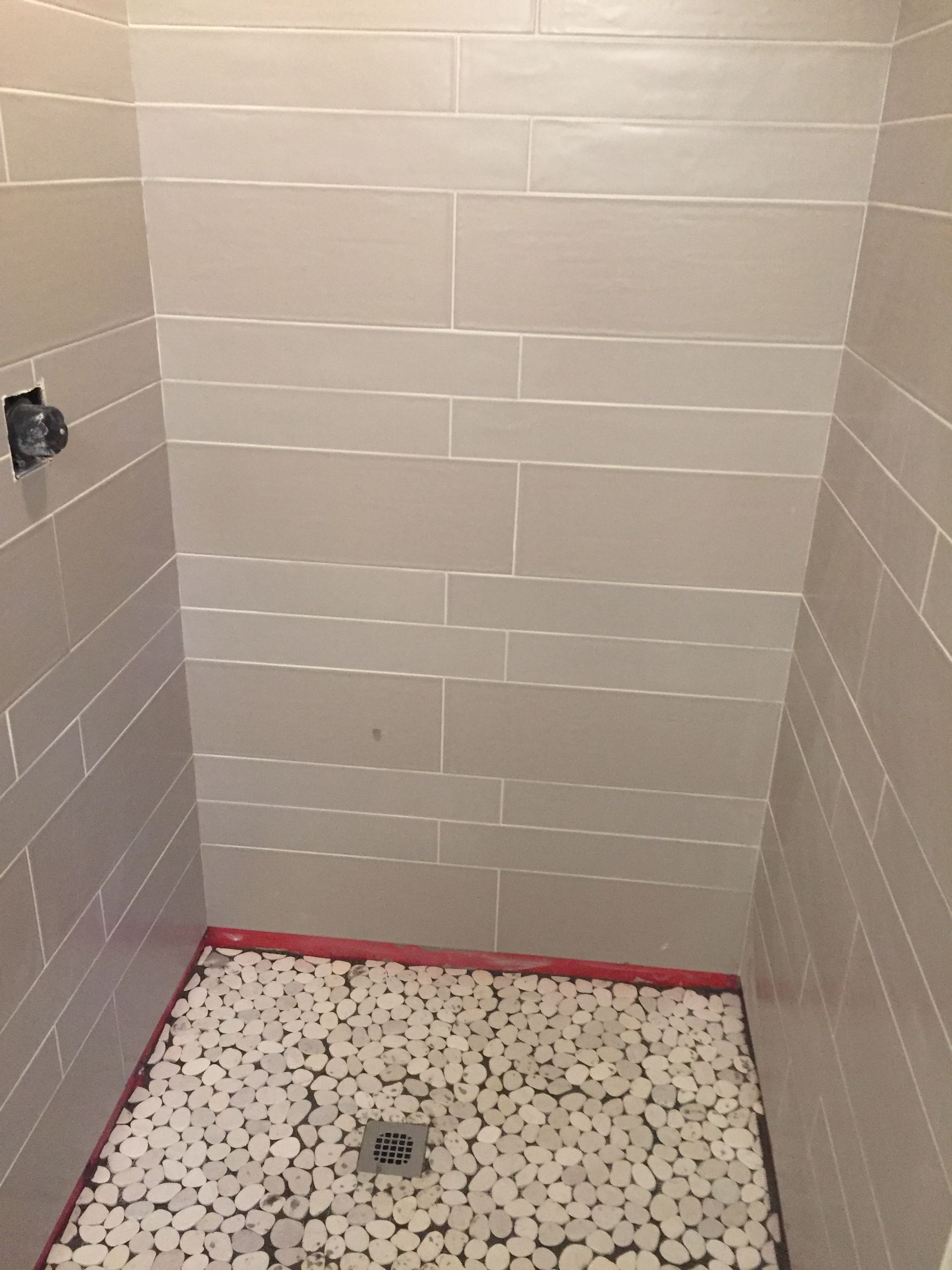 A shower stall with white tiles and white rocks on the floor.