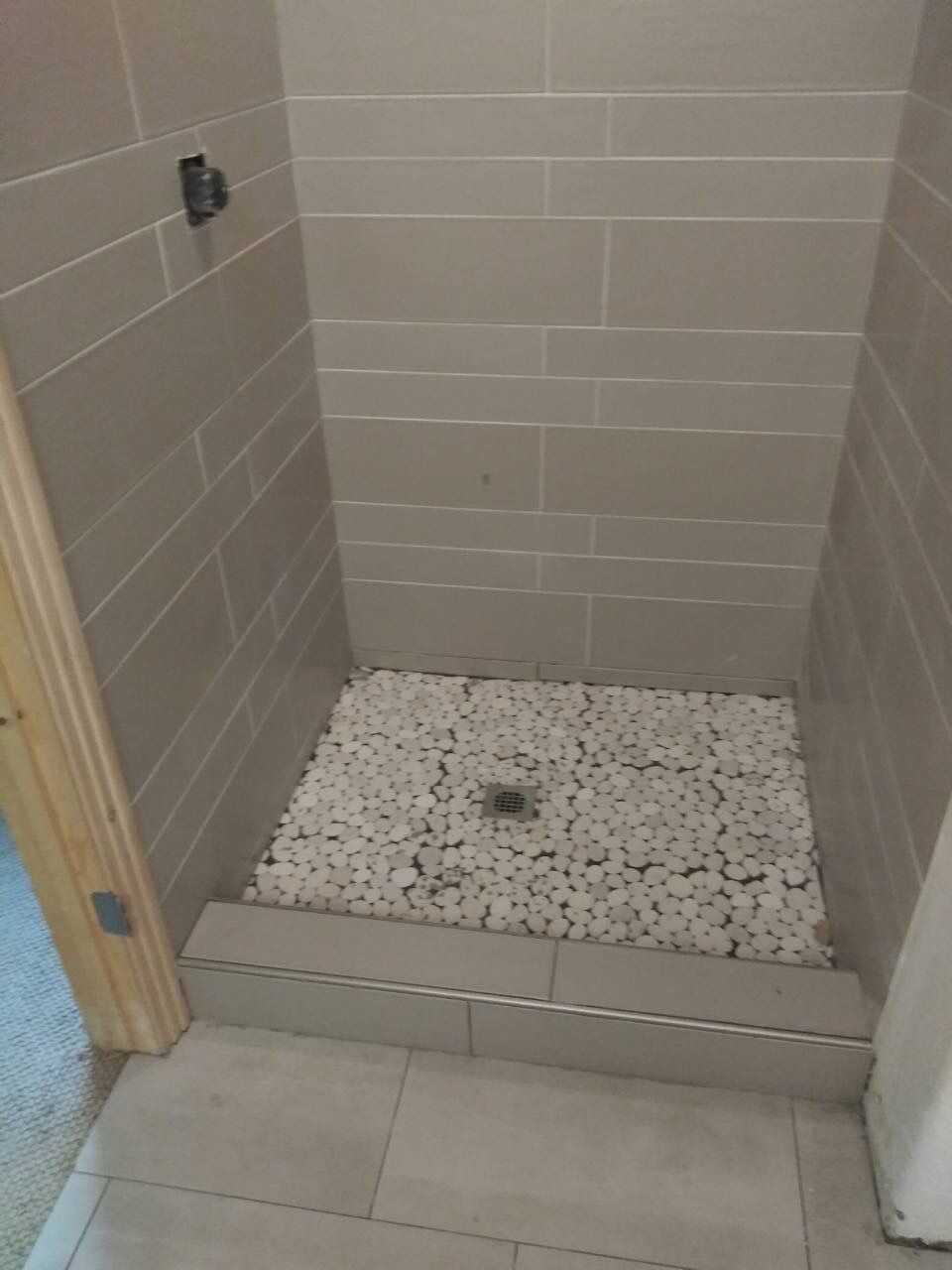 A shower stall with a tiled floor and white rocks in it.