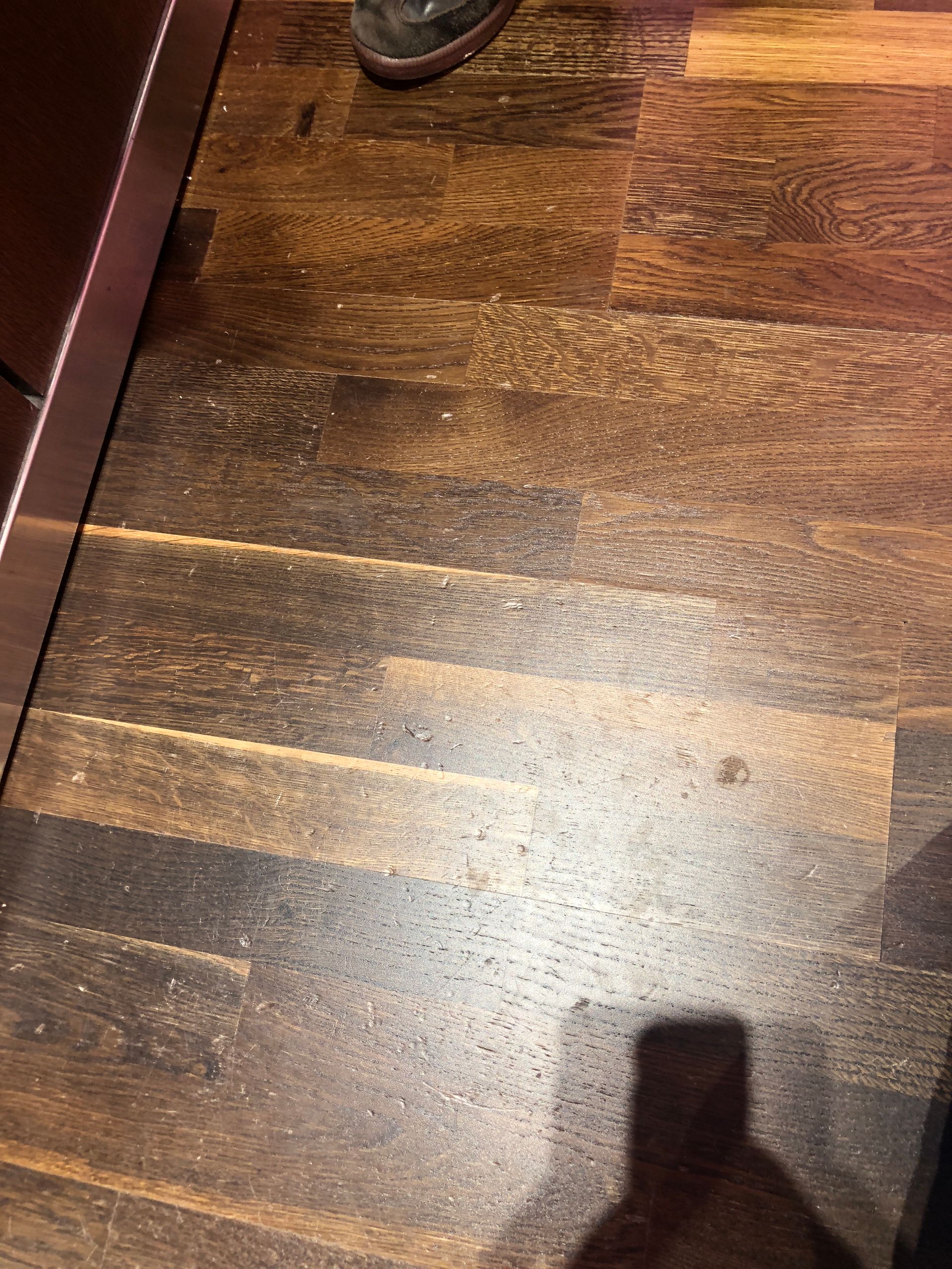 A person is standing on a wooden floor with a shadow on it.